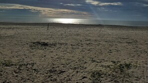 Una playa con una extensa orilla arenosa y una vista despejada del océano bajo un cielo parcialmente nublado.