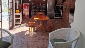 A rustic kitchen with a wooden table, white wicker chairs, and a brick oven.