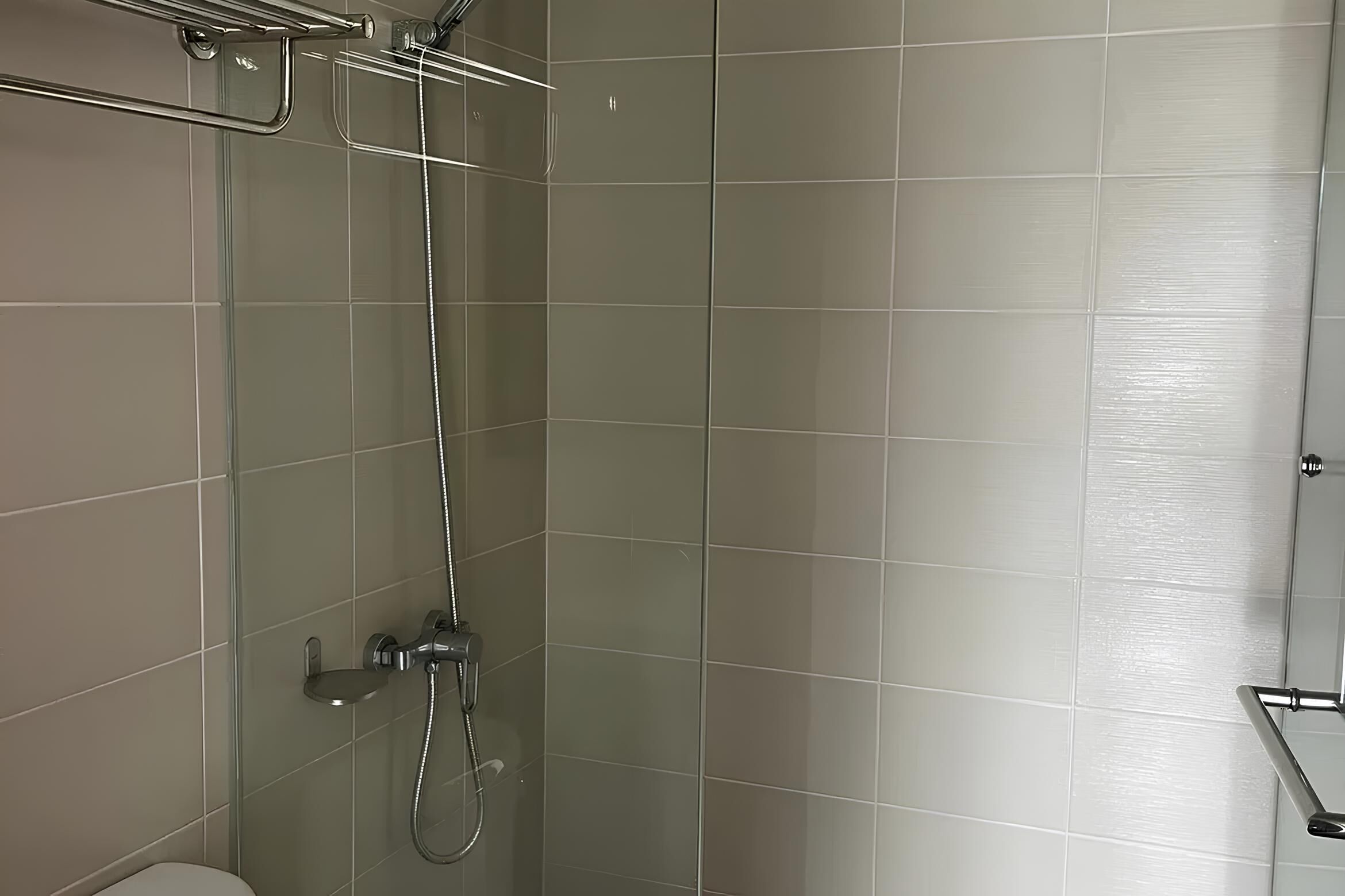 Un baño moderno con cabina de ducha de vidrio, ducha con cabezal cromado y toallero de cromo.