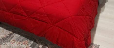 A bedroom with a bed, grey headboard, grey pillows, and a red bedspread.