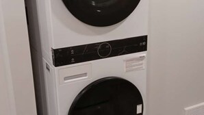 Une machine à laver et un sèche-linge superposés dans une pièce dont le sol et les murs sont de couleur claire.