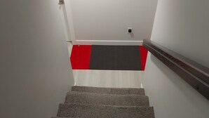 Un escalier dont les marches sont recouvertes de moquette, menant à un palier dont le sol est rouge et blanc.