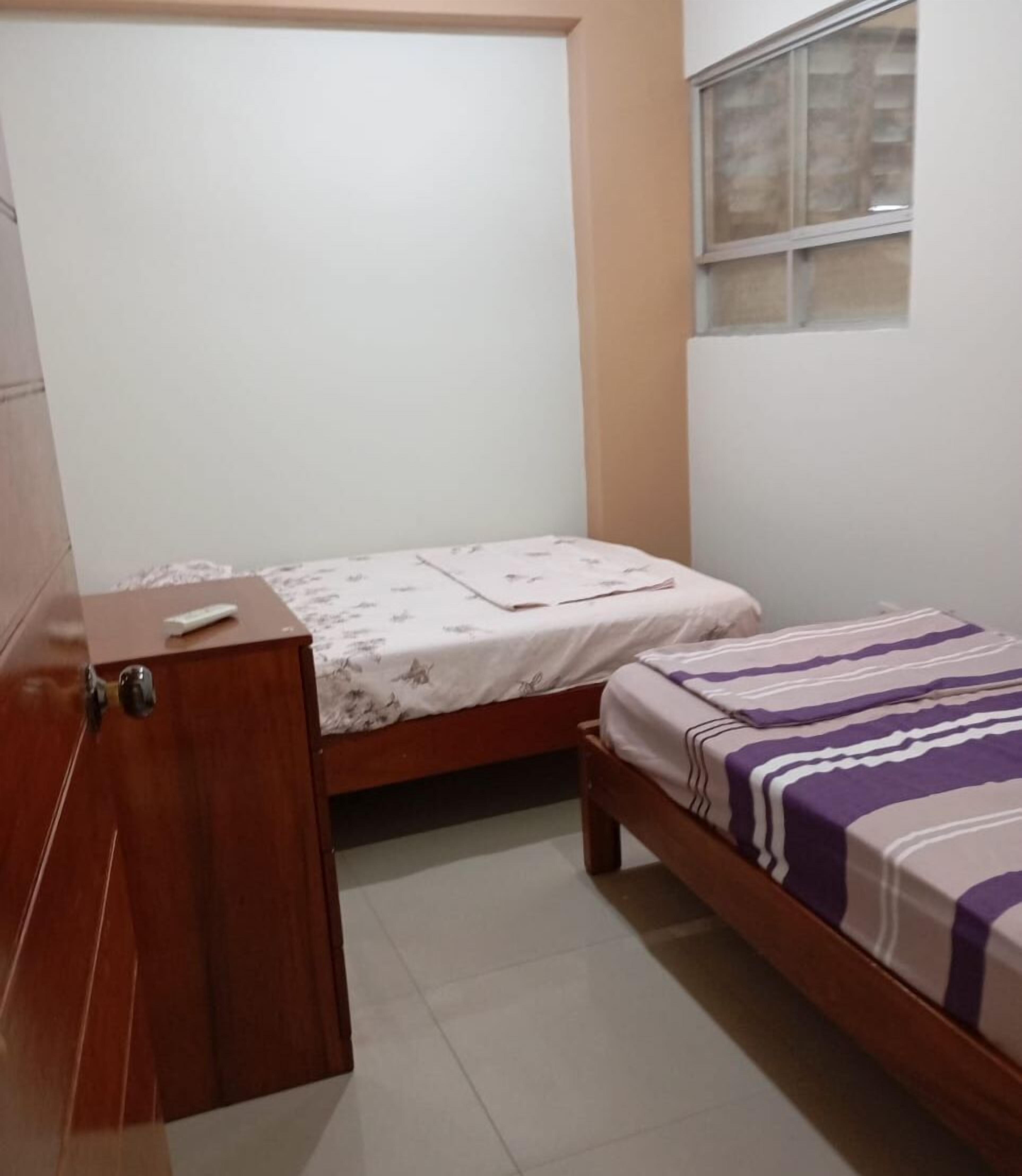 A small bedroom with two beds, a wooden wardrobe, and a window with blinds.