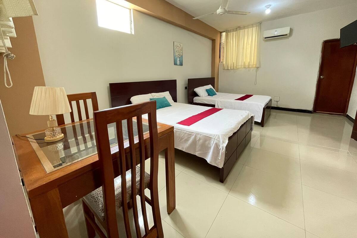 A hotel room with two beds, a desk, a chair, a ceiling fan, and a window.