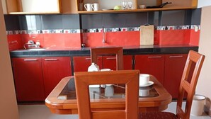 A compact kitchen with red cabinets, a black countertop, and a wooden dining table with chairs. - Apart hotel Emanuel & Cavita  (Iquitos)