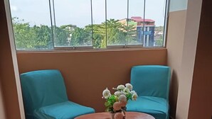 A room with two teal chairs, a wooden table with a flower arrangement, and a view of buildings through large windows. - Apart hotel Emanuel & Cavita  (Iquitos)