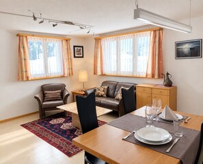 A furnished living room with a sofa, chairs, a dining table set for two, and a rug.