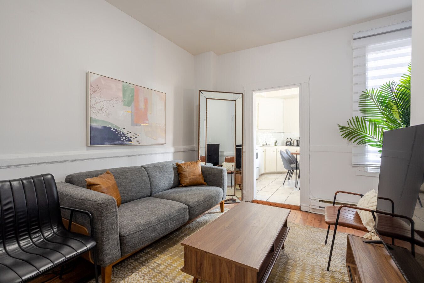 A modern living room with a grey sofa, black chairs, a wooden coffee table, and a large abstract painting on the wall.