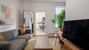 Ein Wohnzimmer mit einer Couch, einem Couchtisch, einem Fernseher und einem Essbereich im Hintergrund.