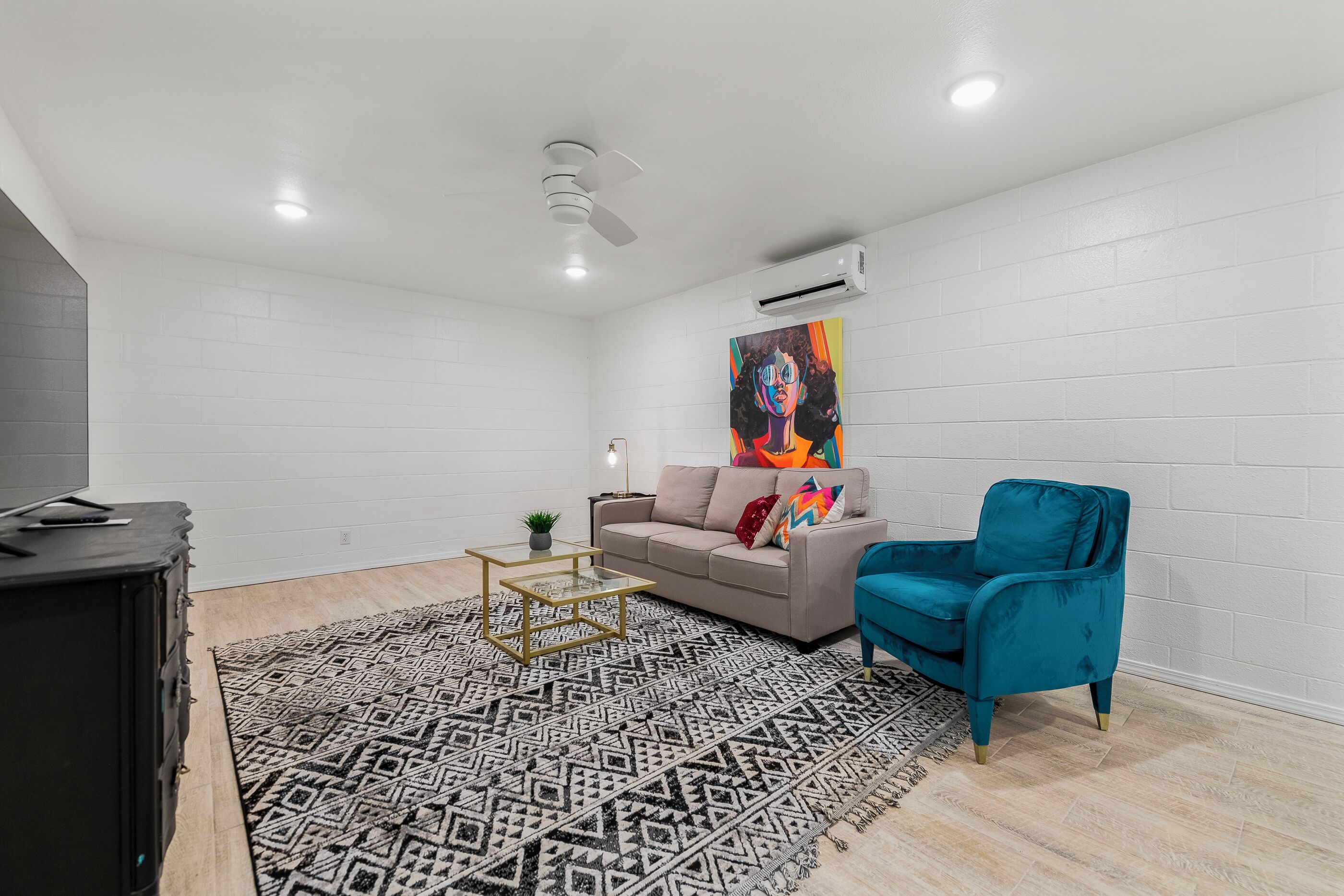 A living room with a sofa, a teal armchair, a patterned rug, a coffee table, and a painting on the wall.