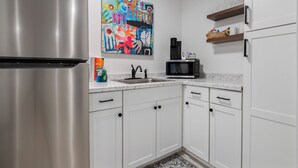 Eine moderne Küche mit weißen Schränken, einem Edelstahl-Kühlschrank, einer Mikrowelle und einem farbenfrohen, abstrakten Gemälde an der Wand.