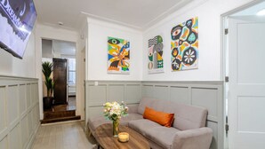 A modern living room with a beige sofa, a wooden coffee table with a vase of flowers, and colorful abstract art on the walls. - The Metro Stay – Vibrant 3BR in Gay Village (Montréal)