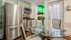 A modern kitchen with stainless steel appliances, a glass dining table, and a view of a green garden through a door. - The Metro Stay – Vibrant 3BR in Gay Village (Montréal)