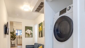 Ett tvättrum med staplade tvättmaskiner och torktumlare, en soffa och en hall som leder till ett vardagsrum.