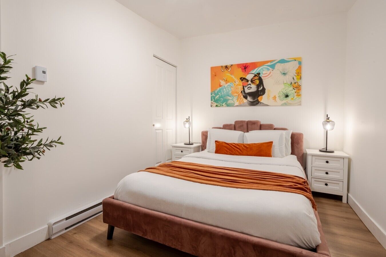Un dormitorio con cama, mesitas de noche, un cuadro en la pared y una planta en maceta.