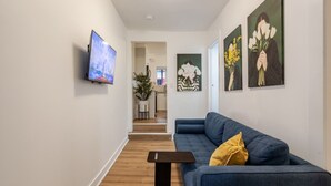 En hall med en blå soffa, en tv och konstverk på väggarna.