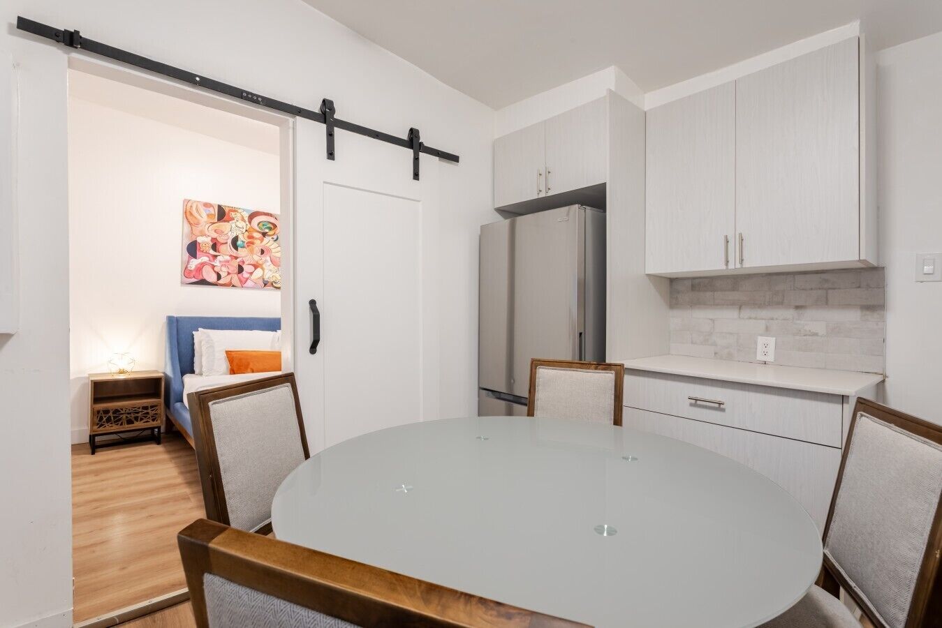 A modern kitchen with white cabinets, a refrigerator, and a dining area with a round table and chairs.