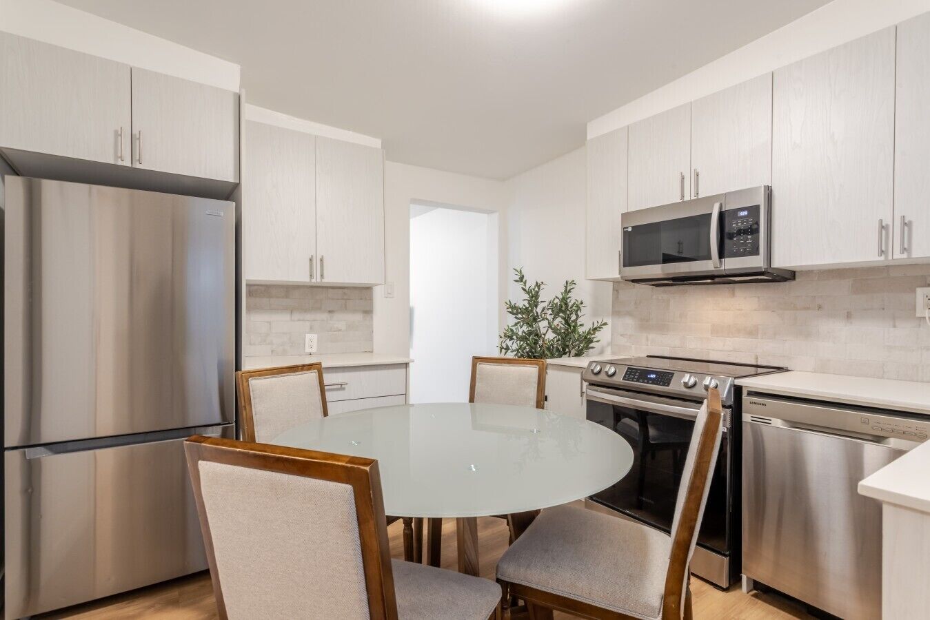 A modern kitchen with stainless steel appliances, a round glass table, and wooden chairs.