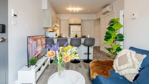 A modern living room with a sofa, a coffee table, a TV, and a kitchen in the background. - The Prestige 3BR| Griffintown Views (Montréal)