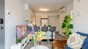 Un salon moderne avec un canapé, une table basse, un téléviseur et une cuisine en arrière-plan.