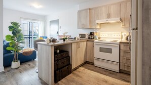 A compact kitchen with wooden cabinets, a built-in oven, and a microwave. - The Prestige 3BR| Griffintown Views (Montréal)