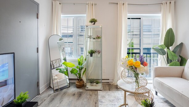 Een moderne woonkamer met een bank, een televisie, een grote spiegel en een plantenarrangement.