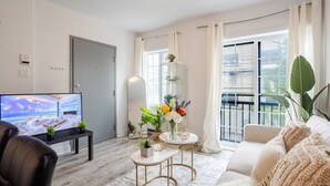 Een moderne woonkamer met een televisie, een bank, een salontafel en een groot raam met gordijnen.