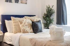 A neatly made bed with a blue headboard, white and beige pillows, and a white throw blanket. - Fashionable 3BR in Griffintown (Montréal)