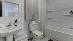 Ein modernes Badezimmer mit einem weißen Waschbecken, einer Toilette und einer Badewanne. Über der Toilette befindet sich ein Holzschrank und eine Duschvorhang.