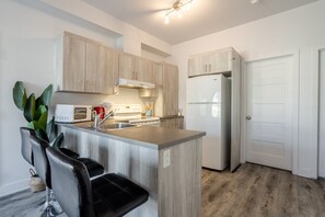 A modern kitchen with wooden cabinets, a stainless steel refrigerator, a built-in island with seating, and a white door.