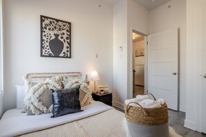 Une chambre à coucher avec un lit, une table de chevet, une lampe et un panier en osier.