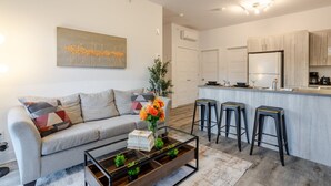 A modern living room with a sofa, coffee table, and bar stools. There is a kitchen area with a countertop and cabinets. - Chic and Spacious 3 Bedrooms in Griffintown (Montréal)
