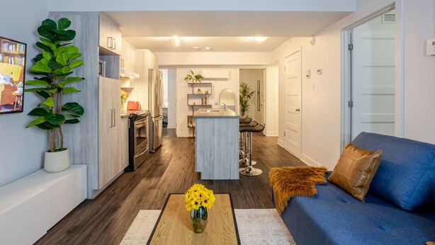A modern living room with a blue sofa, a coffee table with flowers, and a kitchen in the background. - Amazing 4 Bedroom Unit in Downtown (Montréal)
