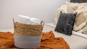 A woven basket with towels on a bed with a brown blanket and a grey pillow. - Amazing 4 Bedroom Unit in Downtown (Montréal)