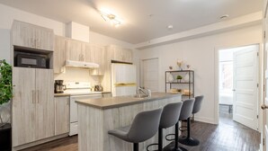A modern kitchen with a central island, bar stools, and a built-in microwave. - Luxurious 4 BR Suite in Griffintown (Montréal)