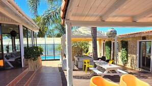 A covered outdoor area with a pool, lounge chairs, and steps leading to a building.