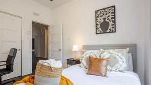 Une chambre d’hôtel avec un lit, une table de chevet, une lampe, une chaise et une porte.