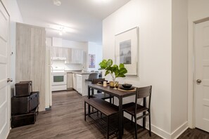 Une cuisine moderne avec des meubles blancs, une table à manger avec des chaises et une plante en pot.