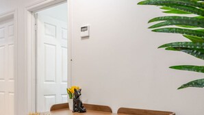 Ein kleiner, moderner Raum mit einem Holztisch, einem kuscheligen Sessel, einer Topfpflanze und einem Thermostat an der Wand.