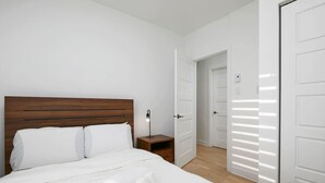 A bedroom with a wooden headboard, a bedside table with a lamp, and a neatly made bed with white linens and towels. - Contemporary 2BR Retreat in MTL`s Gay Village (Montréal)