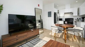 A modern kitchen with white cabinets, a black stove, and a microwave. There is a wooden dining table with four chairs. - Contemporary 2BR Retreat in MTL`s Gay Village (Montréal)