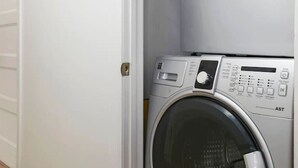 Un lavadero pequeño con lavadora y secadora de carga frontal, una puerta blanca y piso de madera.
