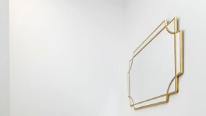 Una esquina con una pared blanca, una mesa de mármol con un jarrón rosa y un espejo con marco dorado.
