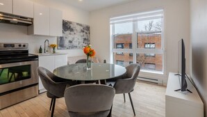 Een moderne keuken met een ronde glazen tafel, grijze stoelen en een bloemenvaas.