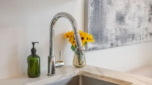 Een badkamermeubel met een modern mengkraan, een groene zeepdispenser en een vaas met gele bloemen.
