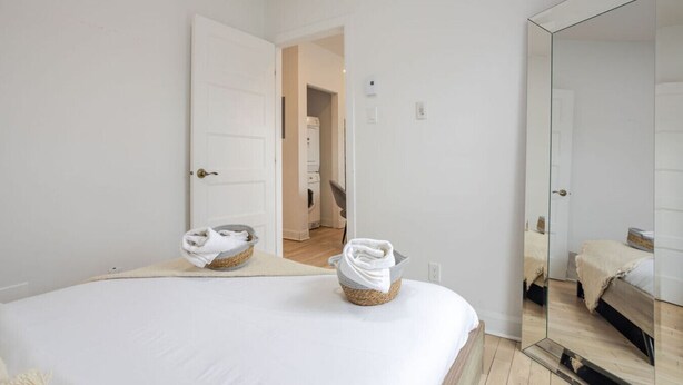 Een strak ingerichte hotelkamer met een groot bed, een spiegel en een deur naar de badkamer.