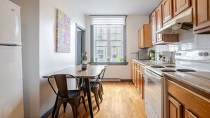 A kitchen with wooden cabinets, a white stove, and a dining table with chairs. - Prime Location | Charming 4BR in Downtown MTL (Montréal)