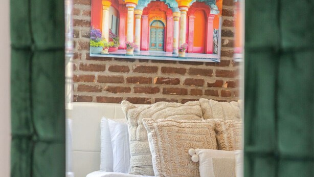 A bed with white bedding and multiple pillows, a brick wall, and a colorful painting above the bed. - Prime Location | Gorgeous 4BR Downtown MTL (Montréal)