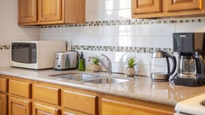 A kitchen with wooden cabinets, a white tiled backsplash, a stainless steel sink, a microwave, a toaster, a coffee maker, and two small potted plants. - Prime Location | Gorgeous 4BR Downtown MTL (Montréal)