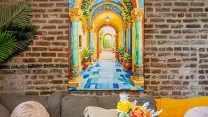 A living room with a large painting of a colorful corridor, a gray sofa, a round coffee table with a vase of flowers, and a brick wall. - Prime Location | Gorgeous 4BR Downtown MTL (Montréal)